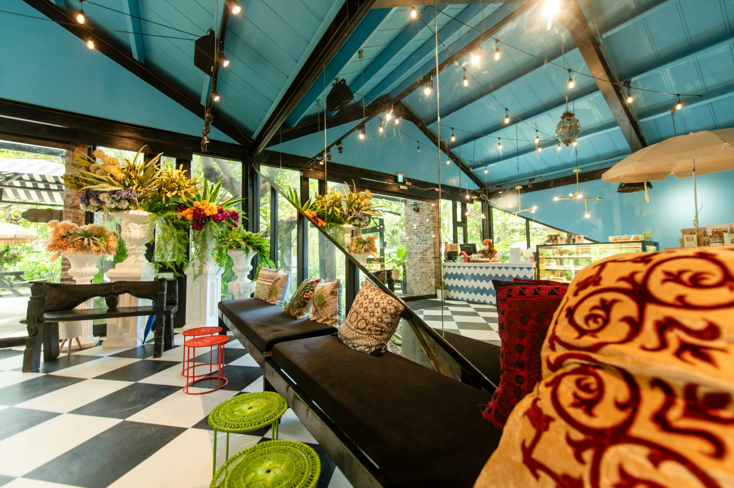 A bright, stylish interior with blue ceilings, black-and-white checkered floors, colorful cushions, and floral arrangements.