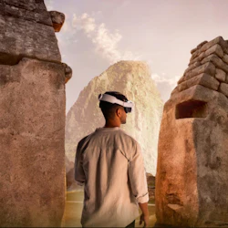 En man med ett VR-headset står bland gamla stenruiner, med ett berg synligt i bakgrunden under en molnig himmel.