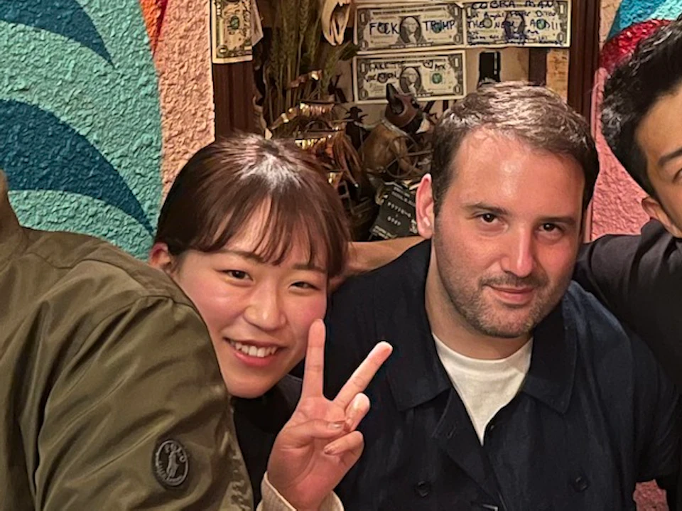A group of five people sitting together in a colorful, decorated room, smiling and posing for the camera with drinks on the table.
