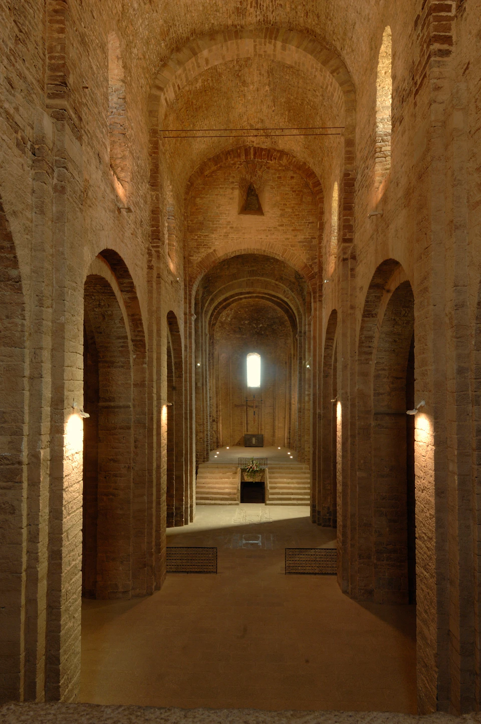 Interior of an ancient, stone church with high arches, a central aisle leading to an altar, and light filtering from a small window.