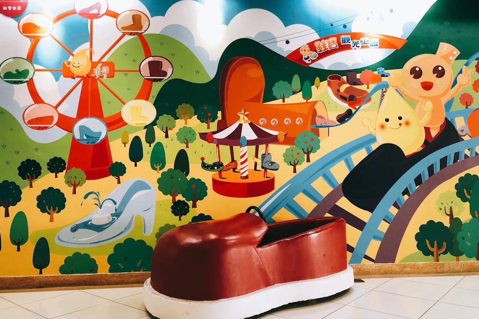 A red shoe-shaped seat in front of a colorful amusement park-themed mural with a ferris wheel and carousel illustrations.