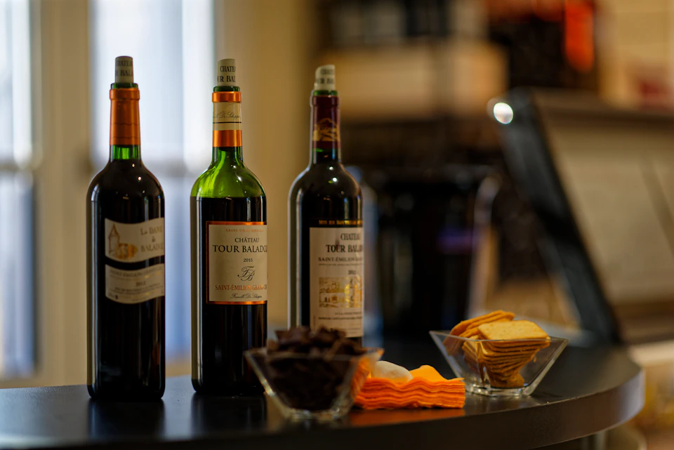 Three wine bottles, two bowls of snacks, and folded napkins on a black surface in a dimly lit setting.