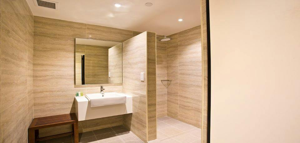 Modern bathroom with a beige tiled design, a sink with a mirror, and a walk-in shower with a rainfall showerhead.