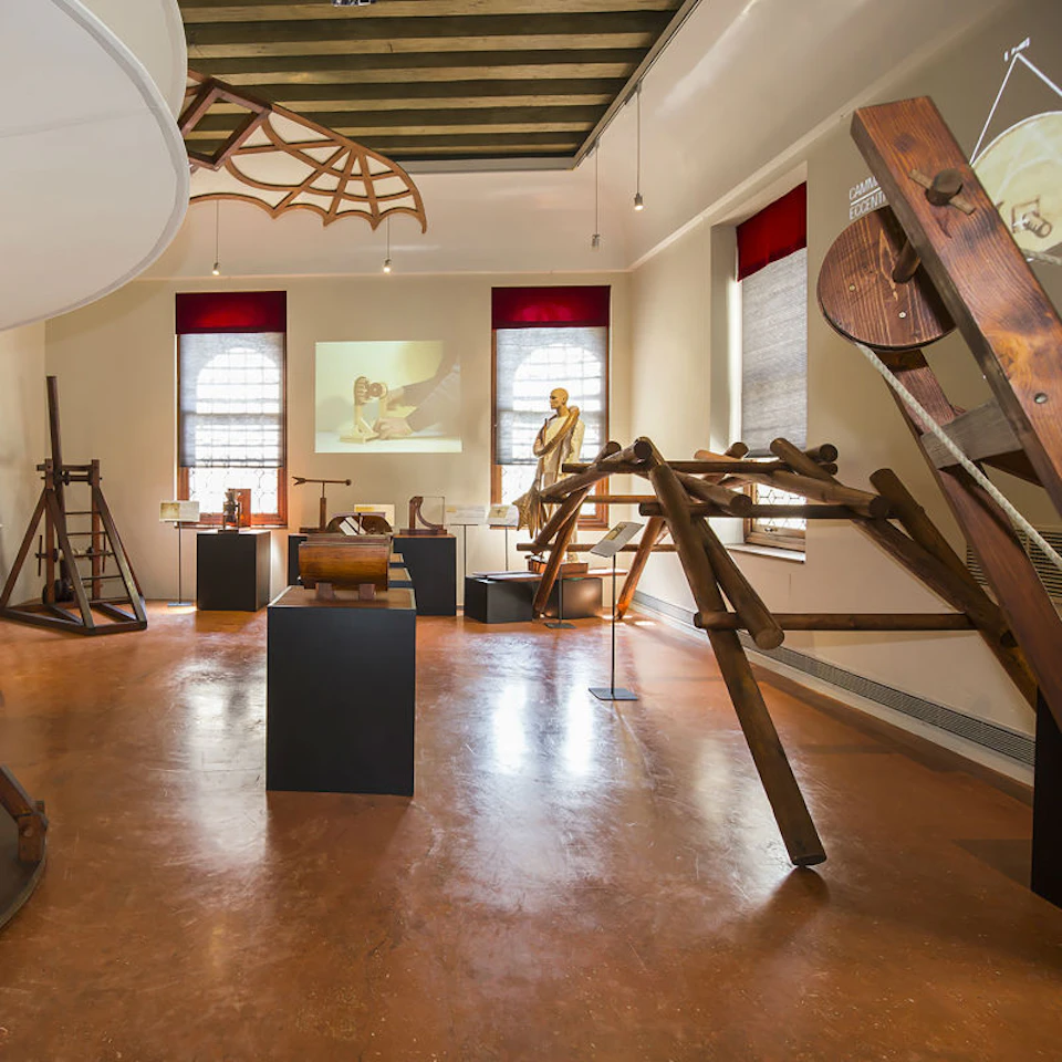 Museum exhibit room featuring historical mechanical inventions, with model displays, a statue, and a projection on the wall.