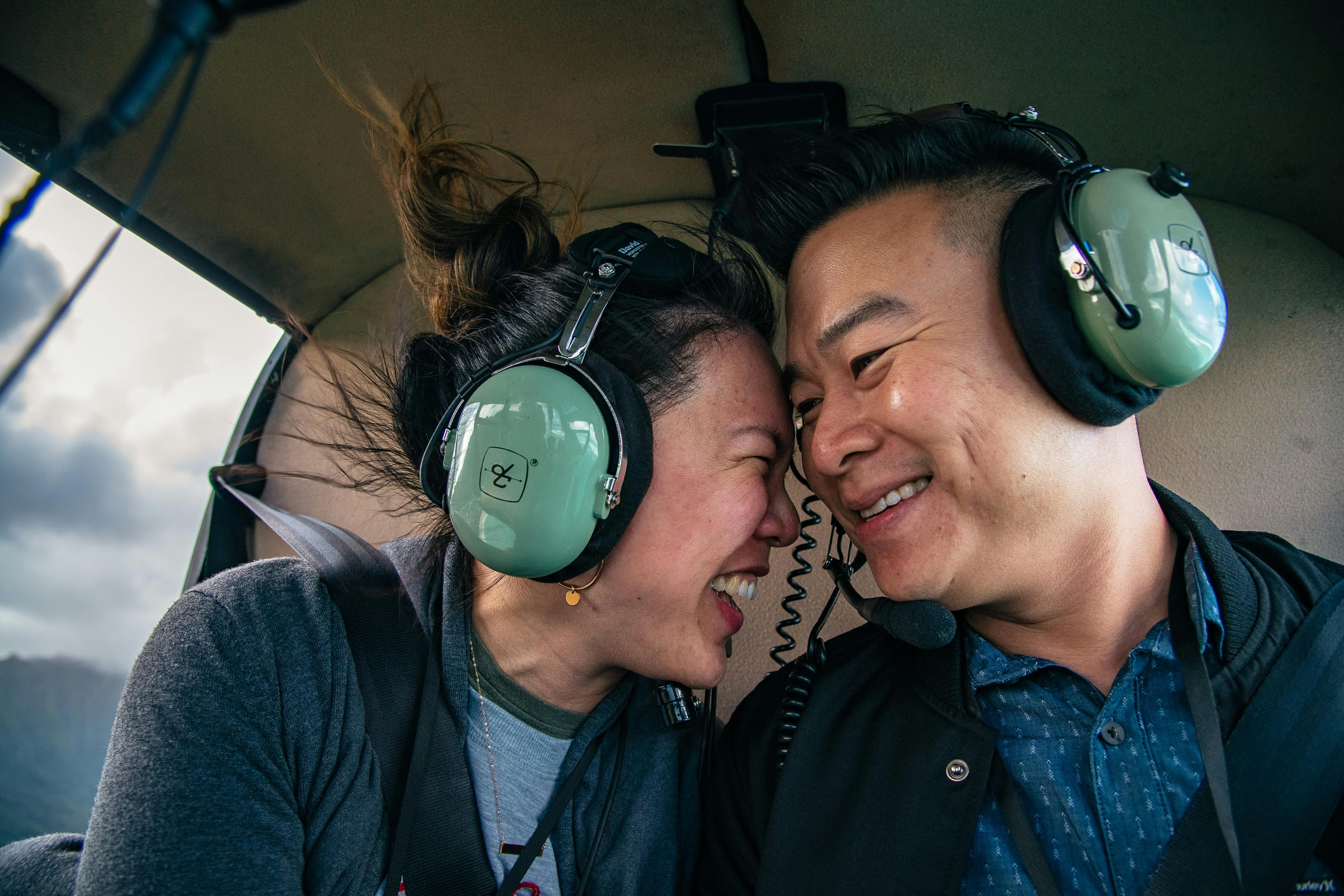 Two people wearing green headphones smile at each other closely inside what appears to be a vehicle or aircraft cabin.
