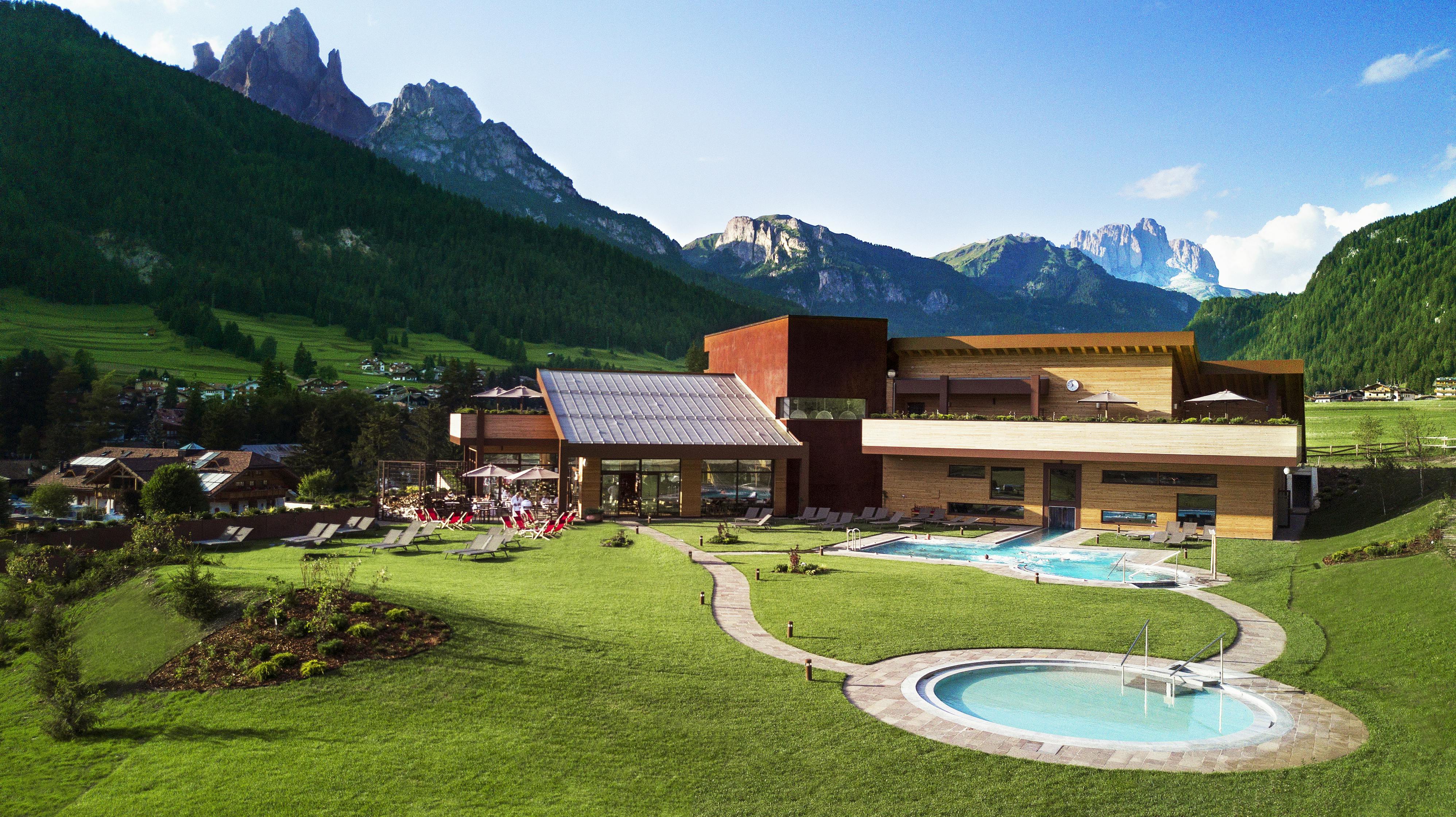 现代度假村设有室外游泳池和草坪，背景是森林覆盖的山脉和晴朗的蓝天。