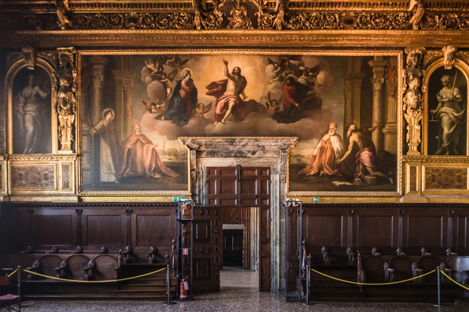 Ornate hall with wooden benches, a large mural depicting biblical scenes, and a wooden doorway. Fire extinguisher visible near the door.