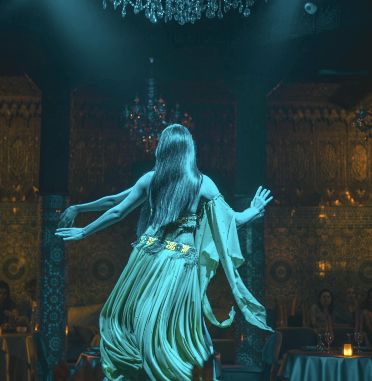 流れるような緑色のドレスを着た女性が、シャンデリアが飾られた薄暗い部屋で優雅に踊っています。