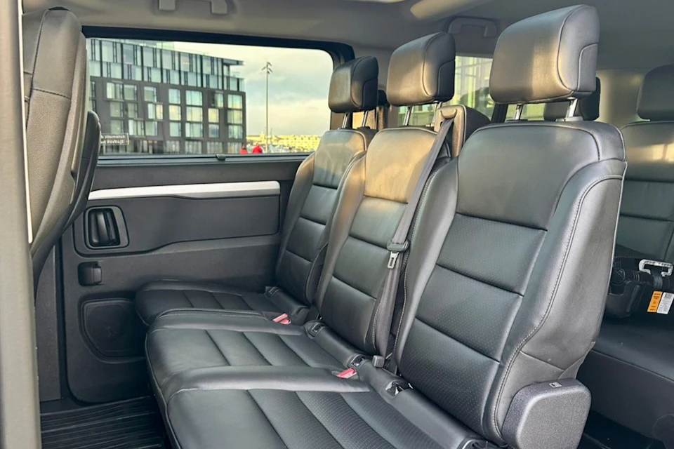 Interior view of a car showcasing black leather back seats with seatbelts, against an urban backdrop seen through windows.