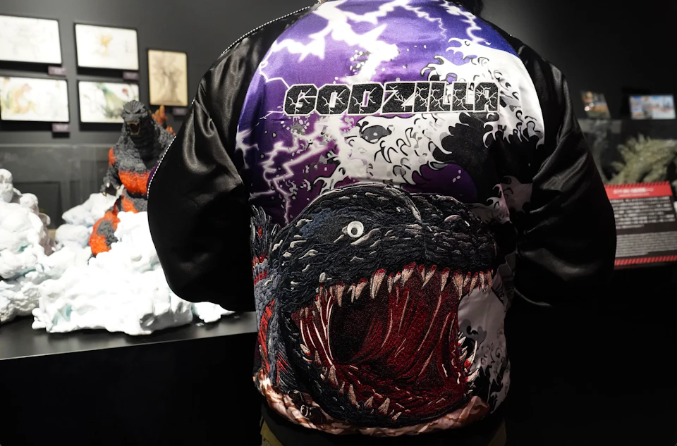 A person wearing a colorful jacket featuring an artistic depiction of Godzilla with the name "Godzilla" written above.