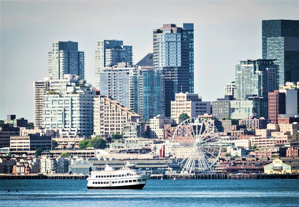 Argosy Cruise boat cruising along the waterfront with the Seattle skyline and Seattle Great Wheel behind it.