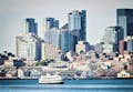 El barco Argosy Cruise navega por el paseo marítimo con el horizonte de Seattle y la Gran Rueda de Seattle detrás.