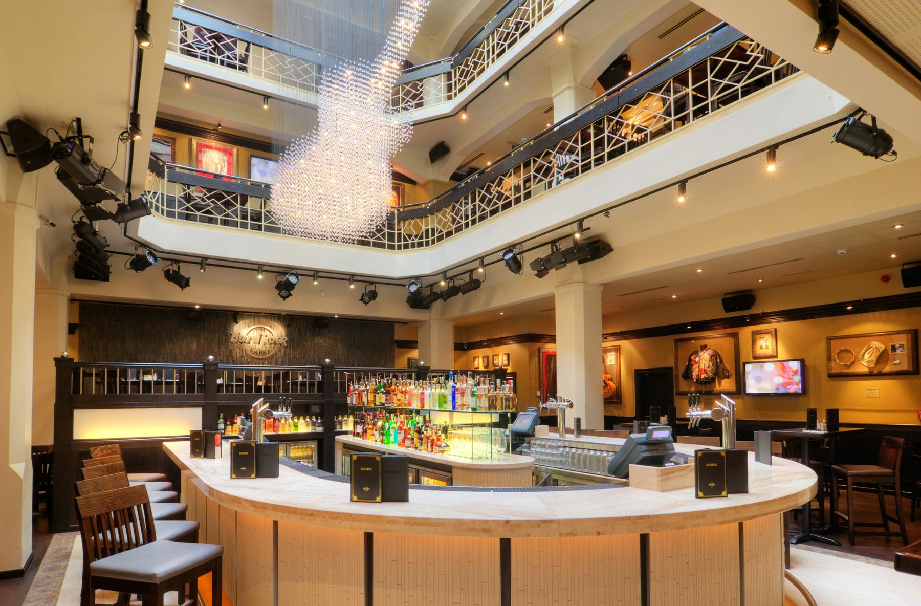 Moderní bar se zakřiveným pultem, lahvemi likéru, vysokými stoličkami a uměleckou výzdobou. Výhled z balkonu v patře se skleněným svítidlem.