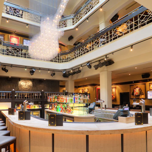 En modern bar med en böjd bänk, spritflaskor, höga pallar och konstnärlig inredning. Balkongutsikt på övervåningen med glasarmatur.