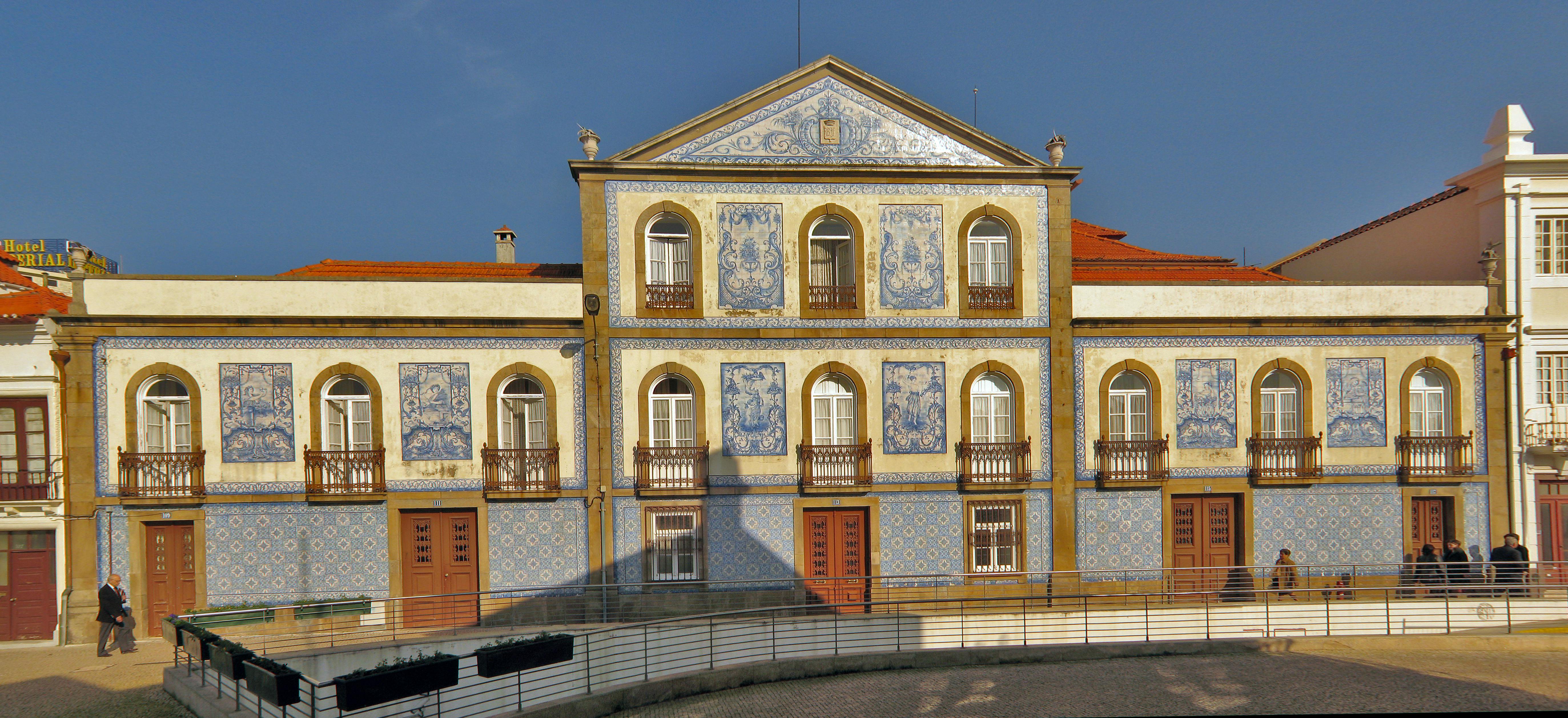 Ornate building with yellow walls, blue tile murals, arched windows with balconies, and a red-tiled roof against a clear sky.