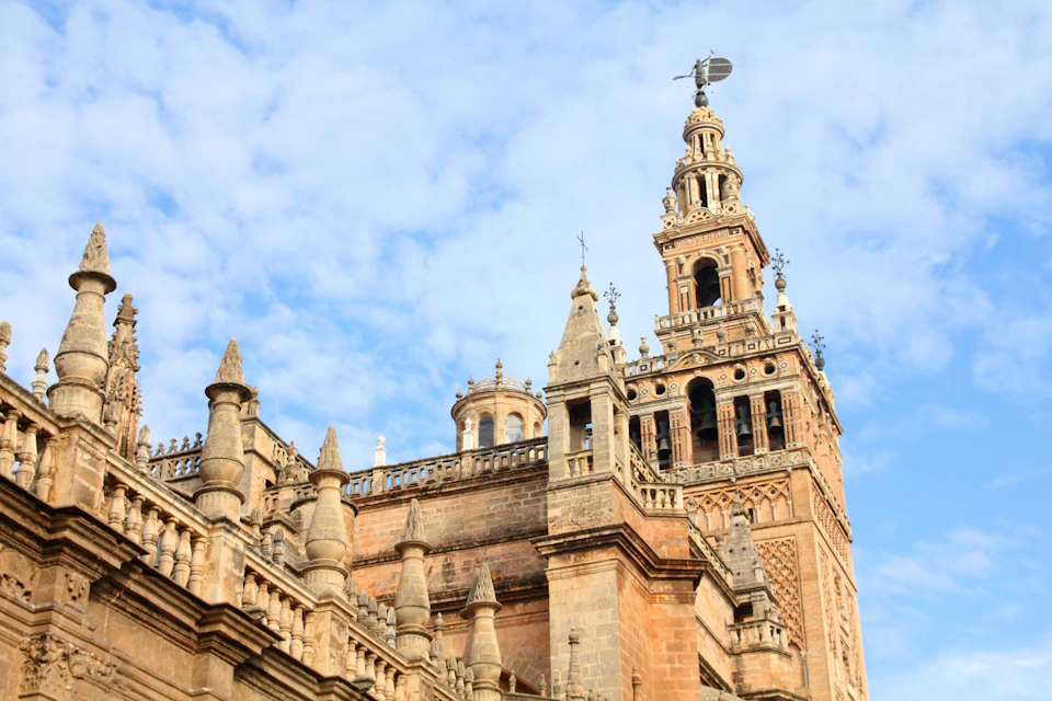 A historic stone bell tower with ornate architecture against a blue sky with scattered clouds.
