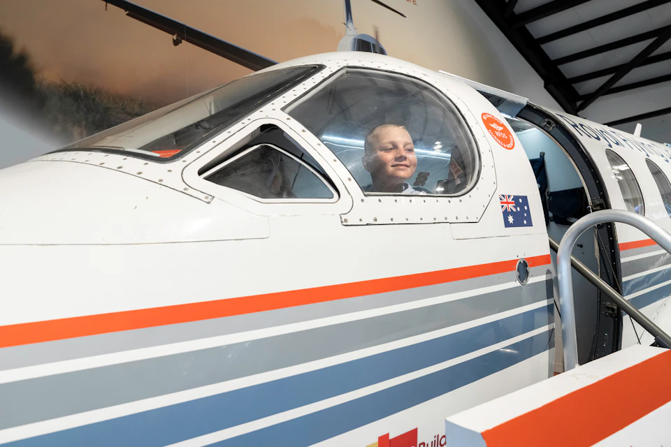 A person peeks through the window of an aircraft cockpit, with visible Australian flag and an open hatch door nearby.