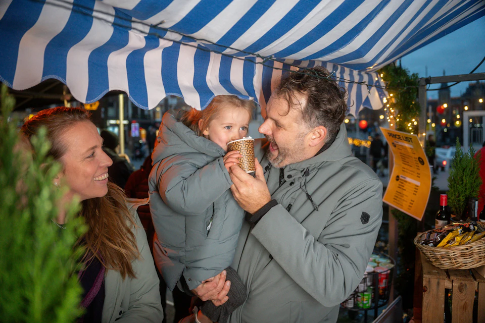 A child enjoying a free cup of hot chocolate being held by her father