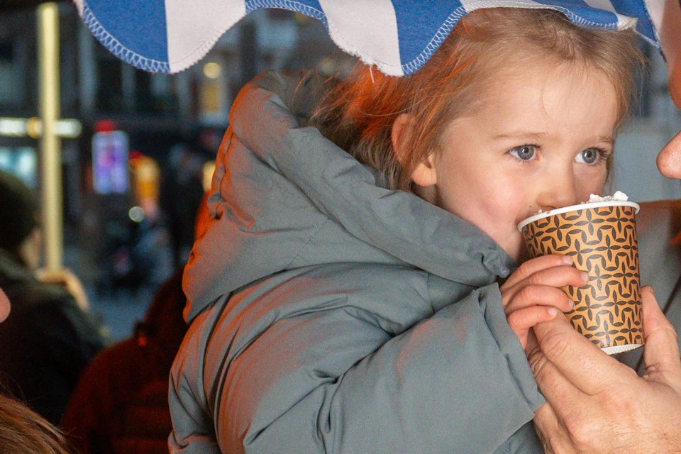 A child enjoying a free cup of hot chocolate being held by her father
