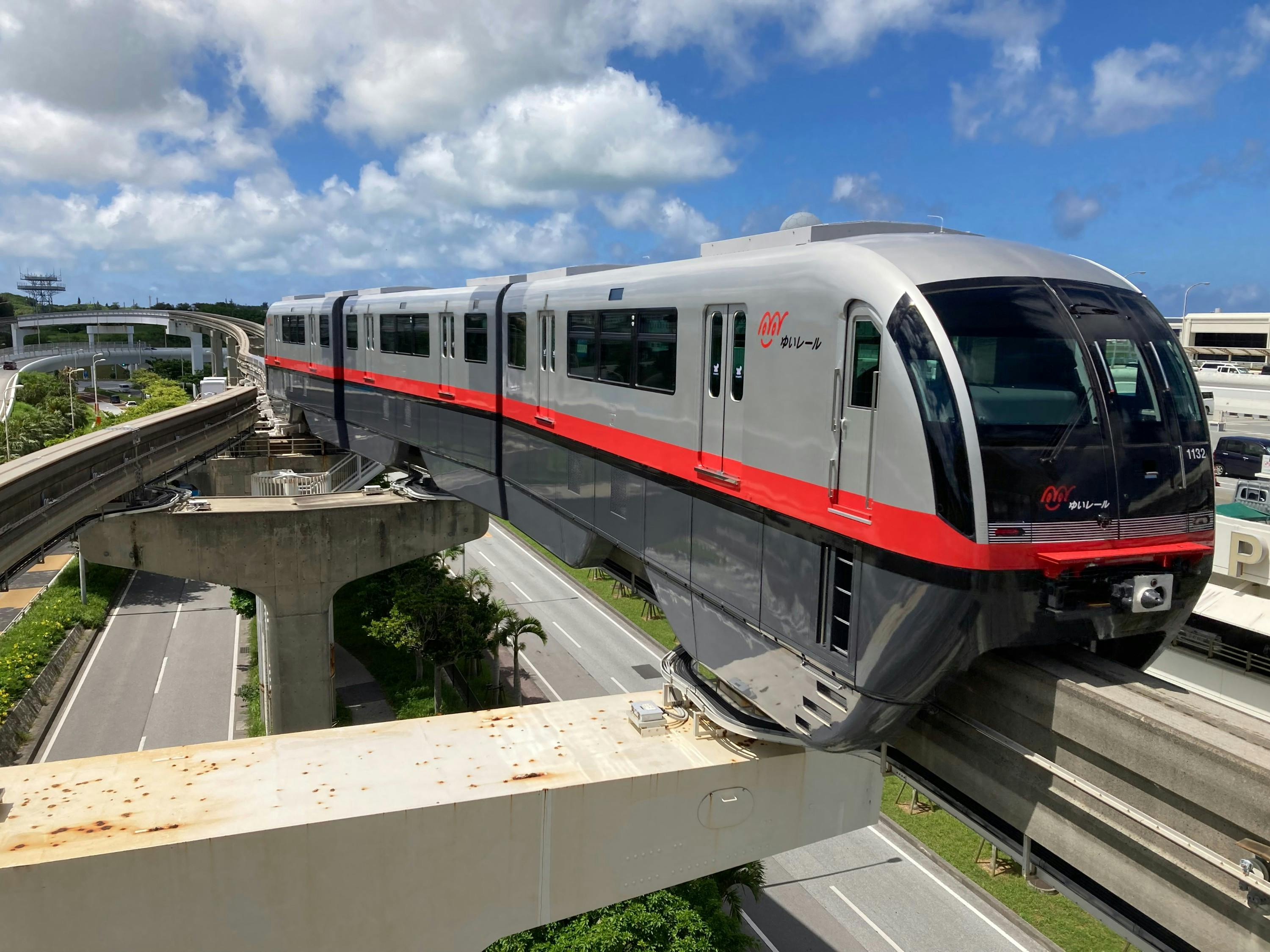Un monorail moderne, orné d'une bande rouge, circulant sur une voie surélevée sous un ciel bleu parsemé de nuages.