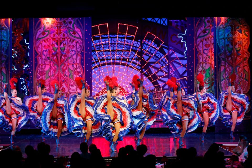 Dancers in colorful costumes performing on a stage with vibrant lighting and a decorative backdrop.