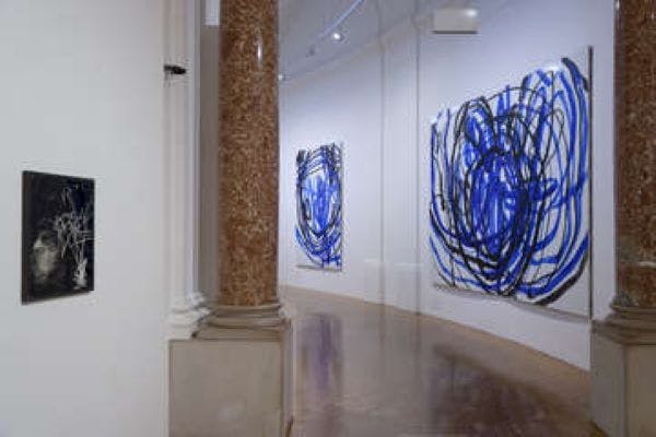Gallery with polished floor, white walls, a brown pillar, and abstract blue and black paintings on display.