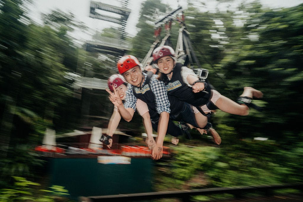 三个戴着头盔和马具的人微笑着穿过郁郁葱葱的绿色户外区域。