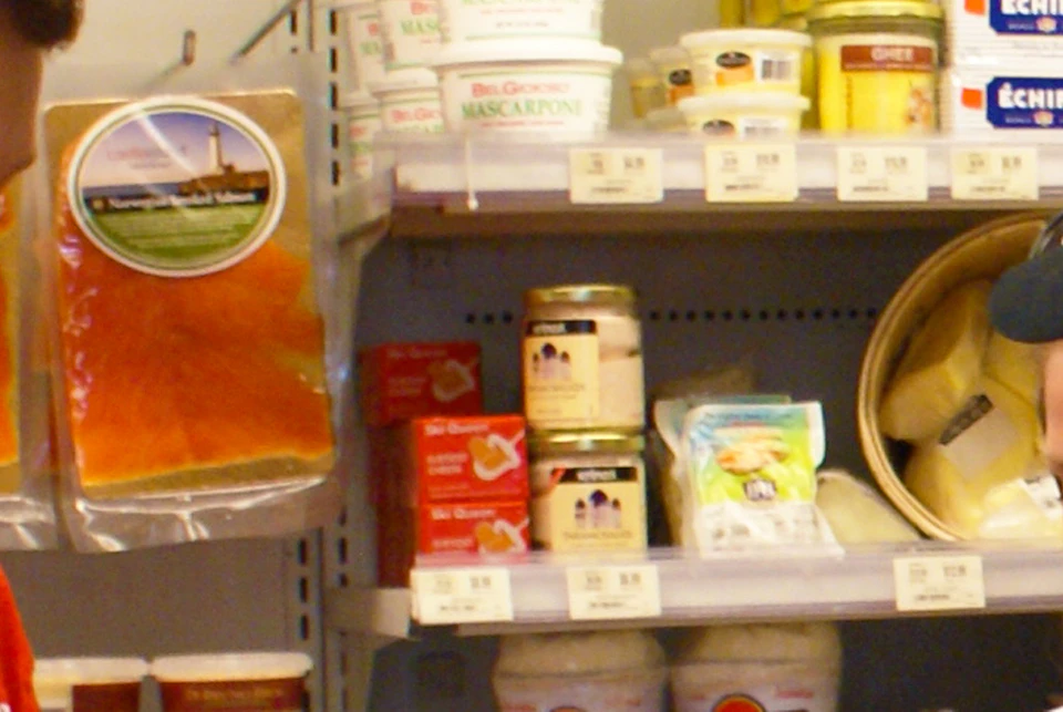 A young man in a red shirt offers food samples to three people in a grocery store aisle filled with dairy products.