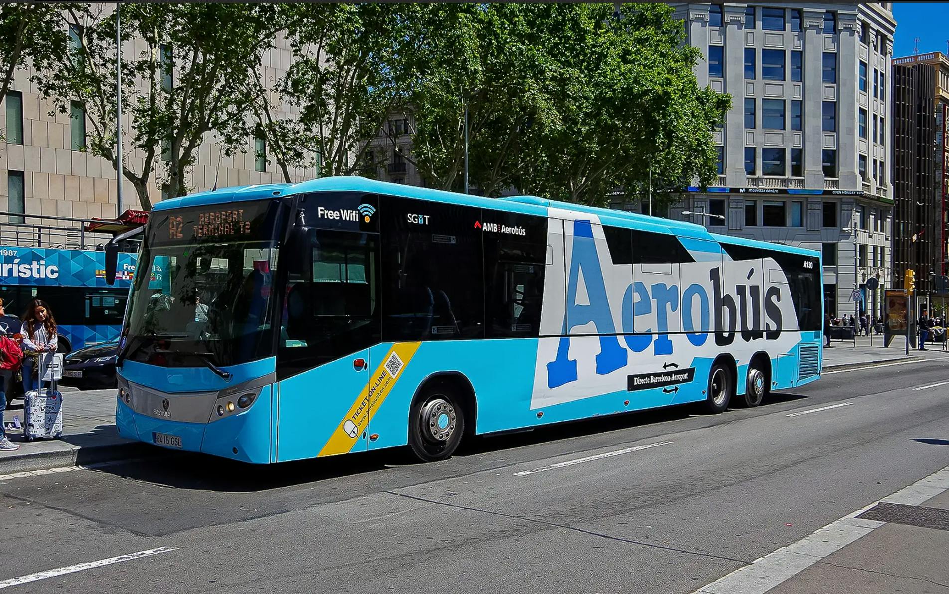 Bus bleu et blanc portant l'inscription "Aerobús" garé dans une rue, offrant le WiFi gratuit, avec des bâtiments et des arbres en arrière-plan.