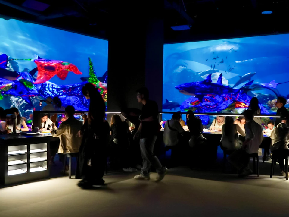 People sitting at tables in a dimly lit room with large, vibrant underwater-themed screens on the walls.