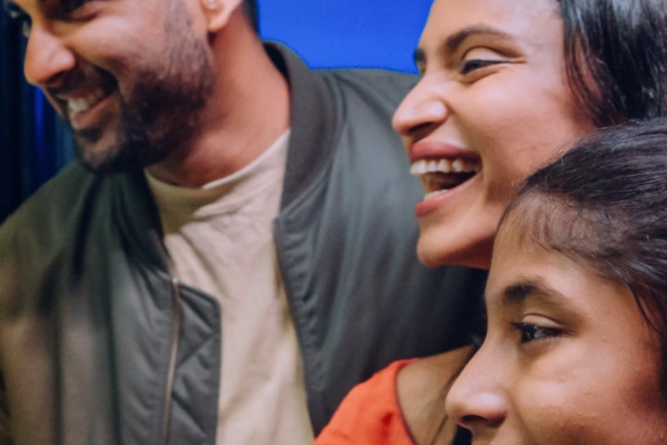 A family of three smiling and observing penguins through a glass enclosure at an indoor aquarium.