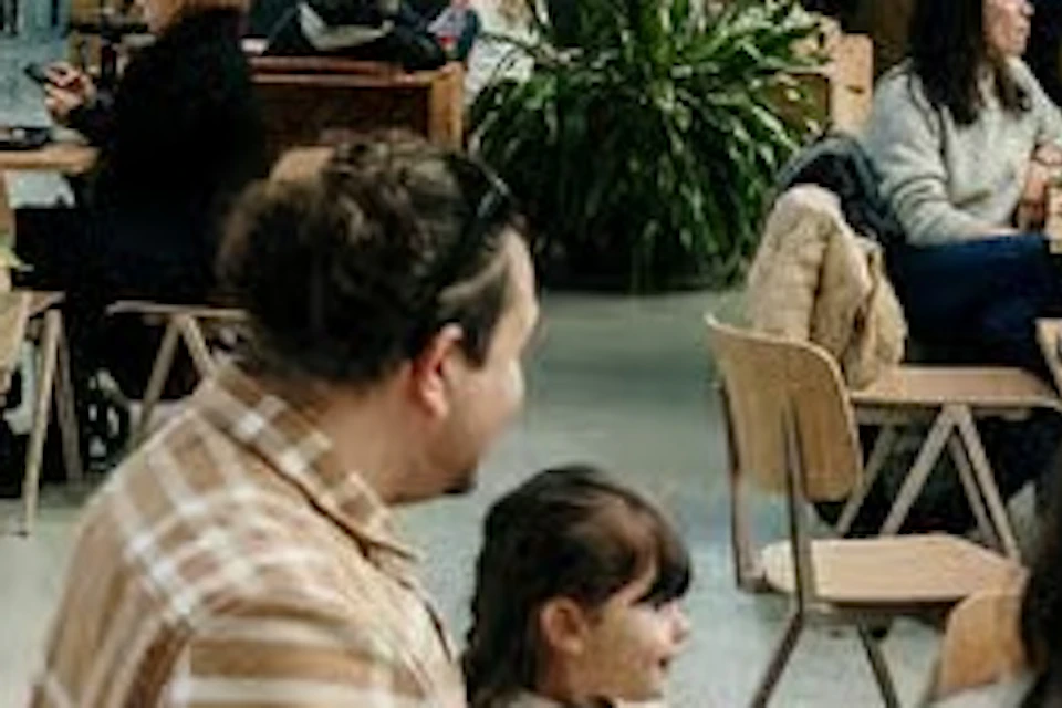 People sitting and talking in a greenhouse-style café with plants and modern decor under a glass ceiling.