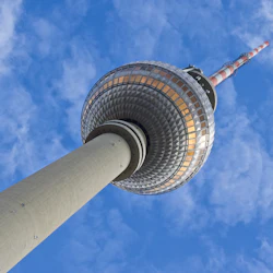 Ett högt TV-torn med ett sfäriskt observationsdäck och en rödrandig antenn som sträcker sig in i en delvis molnig blå himmel.