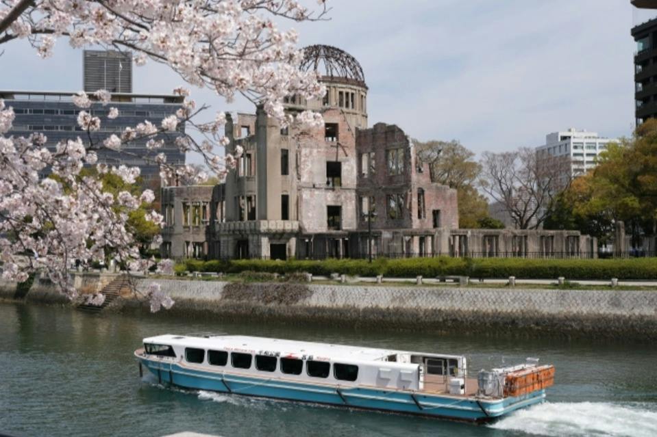 A white boat on a river near the Hiroshima Peace Memorial with cherry blossoms in the foreground.