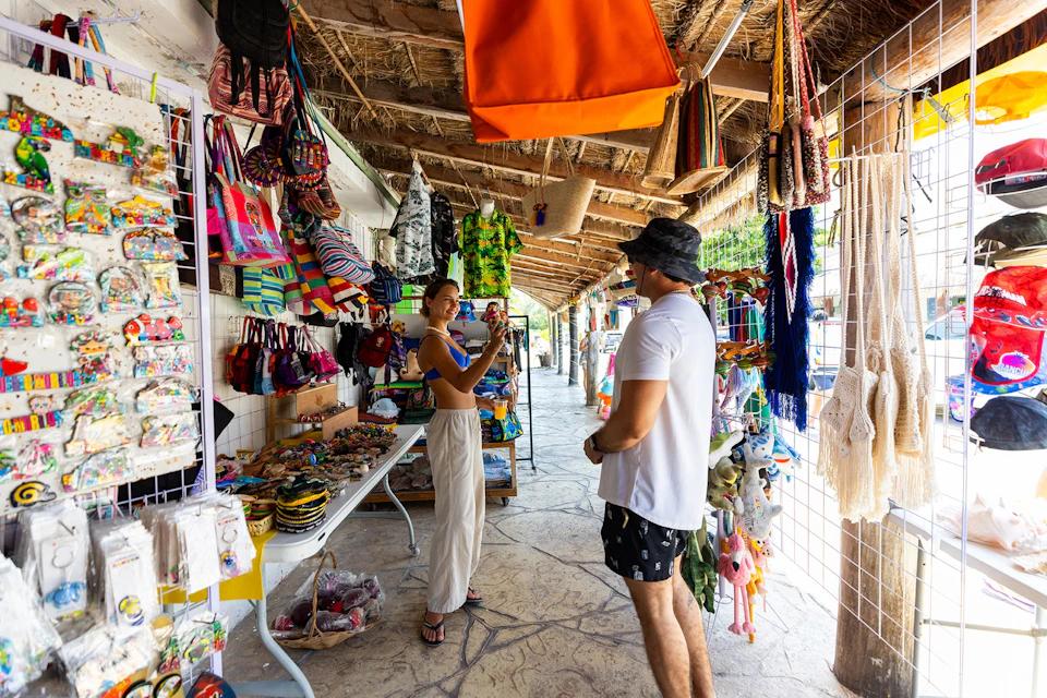 A man and a woman browsing a colorful outdoor market with various bags, clothes, and accessories displayed for sale.
