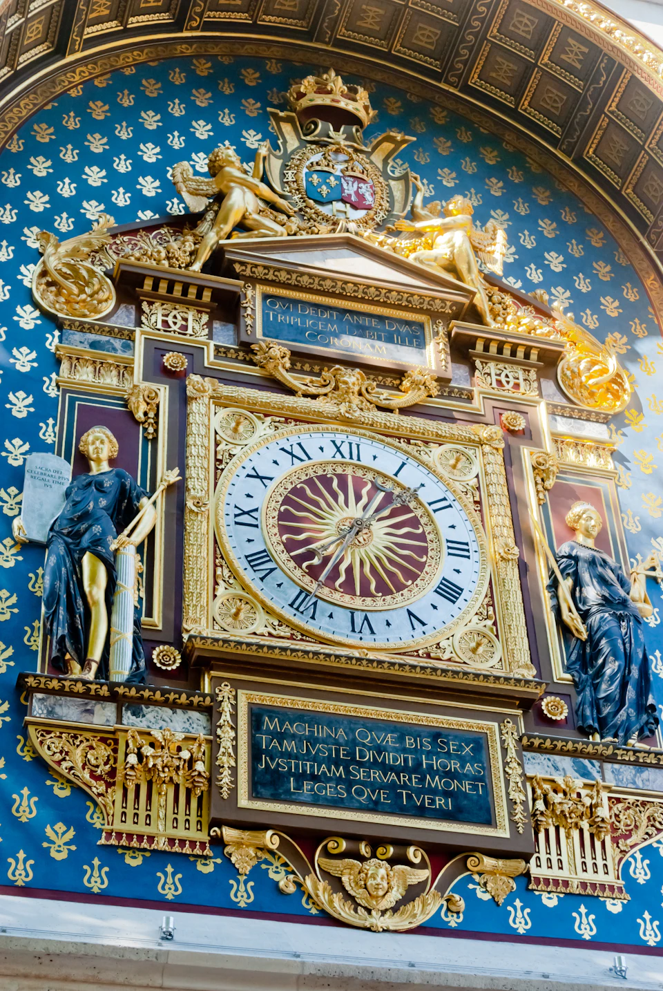 A richly decorated clock with Roman numerals, flanked by two statues, ornate gold elements, and inscriptions in Latin.