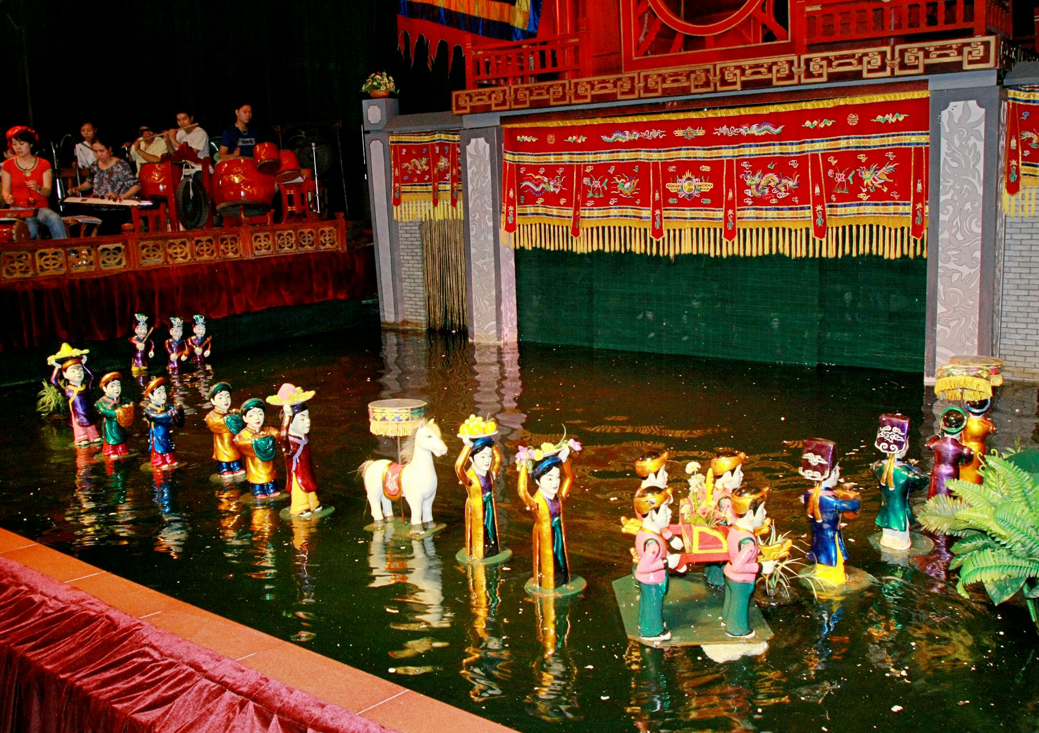 A traditional Vietnamese water puppet performance with puppets on a water stage, colorful costumes, and a red backdrop.