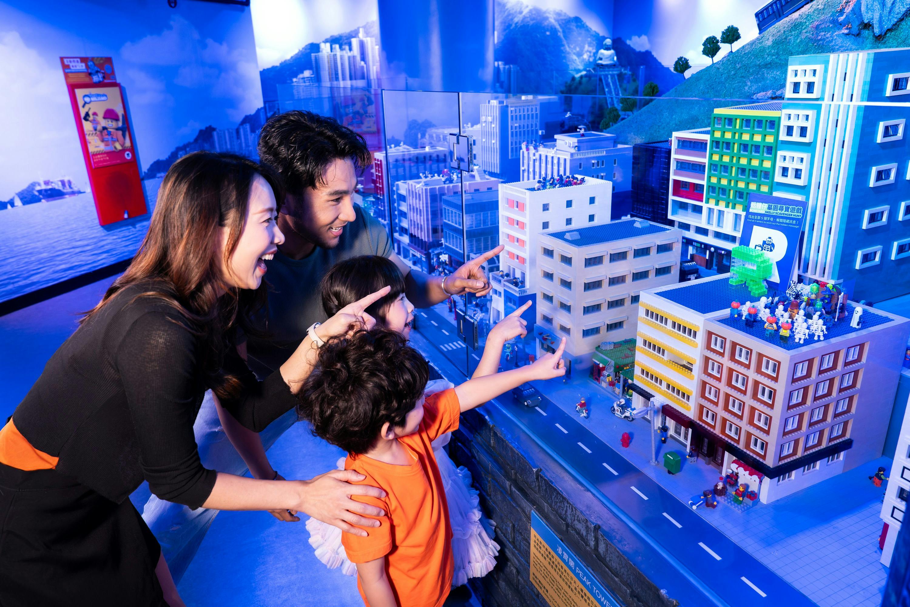 A family of four excitedly pointing at a detailed miniature city model in an indoor exhibit setting.