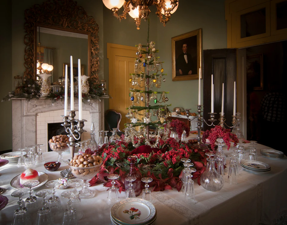 Elegant dining room with a decorated Christmas tree centerpiece, candelabras, glassware, and festive wreaths on a table.