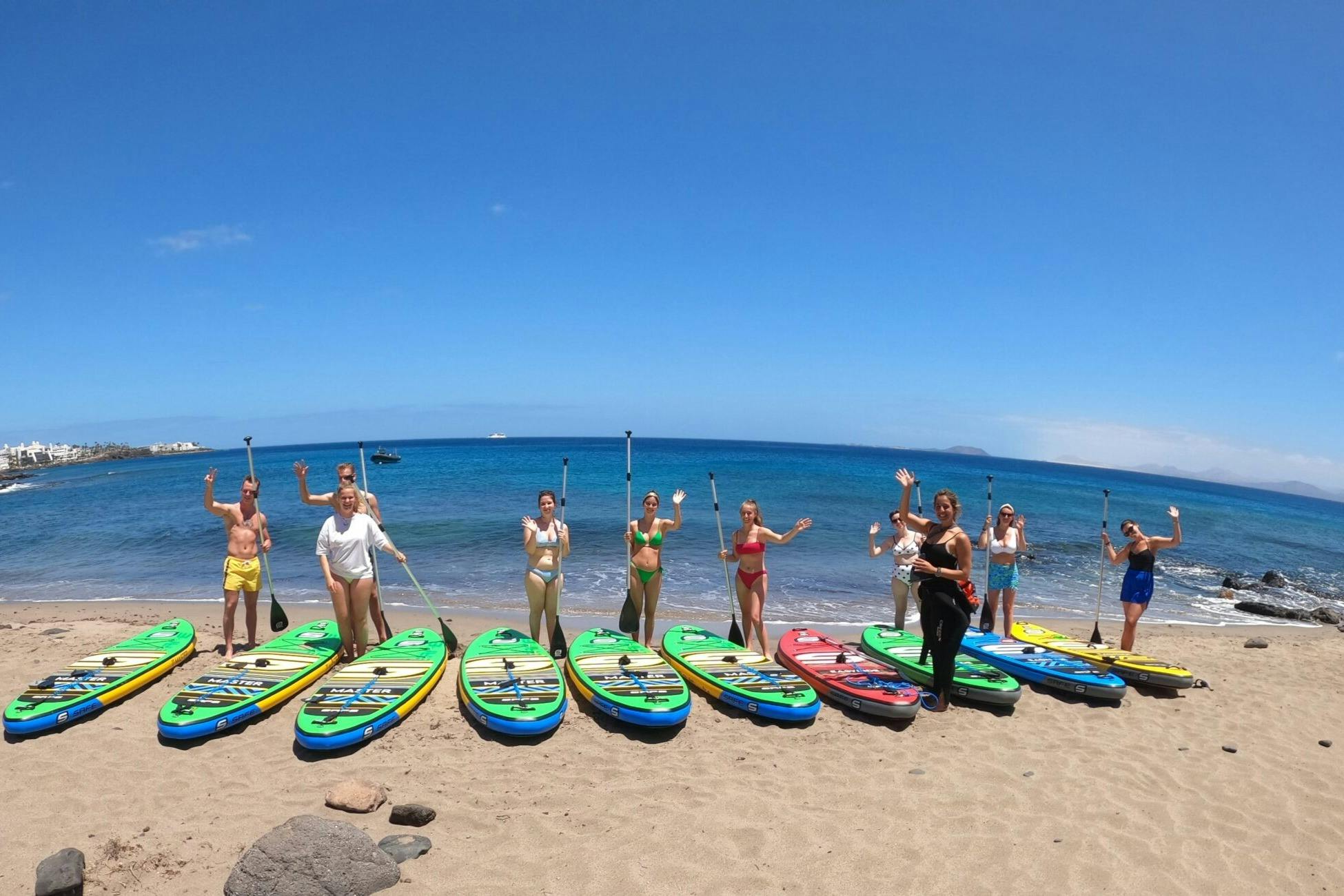 一群穿着泳装的人在海滩上划桨，站在五颜六色的桨板旁边，背景是大海。
