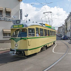 En gul turistspårvagn färdas genom en gata kantad av byggnader och parkerade bilar under en blå himmel med spridda moln.