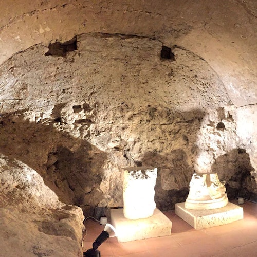 Una stanza poco illuminata con pareti in pietra grezza, con due manufatti in pietra illuminati su piedistalli e faretti sul pavimento.