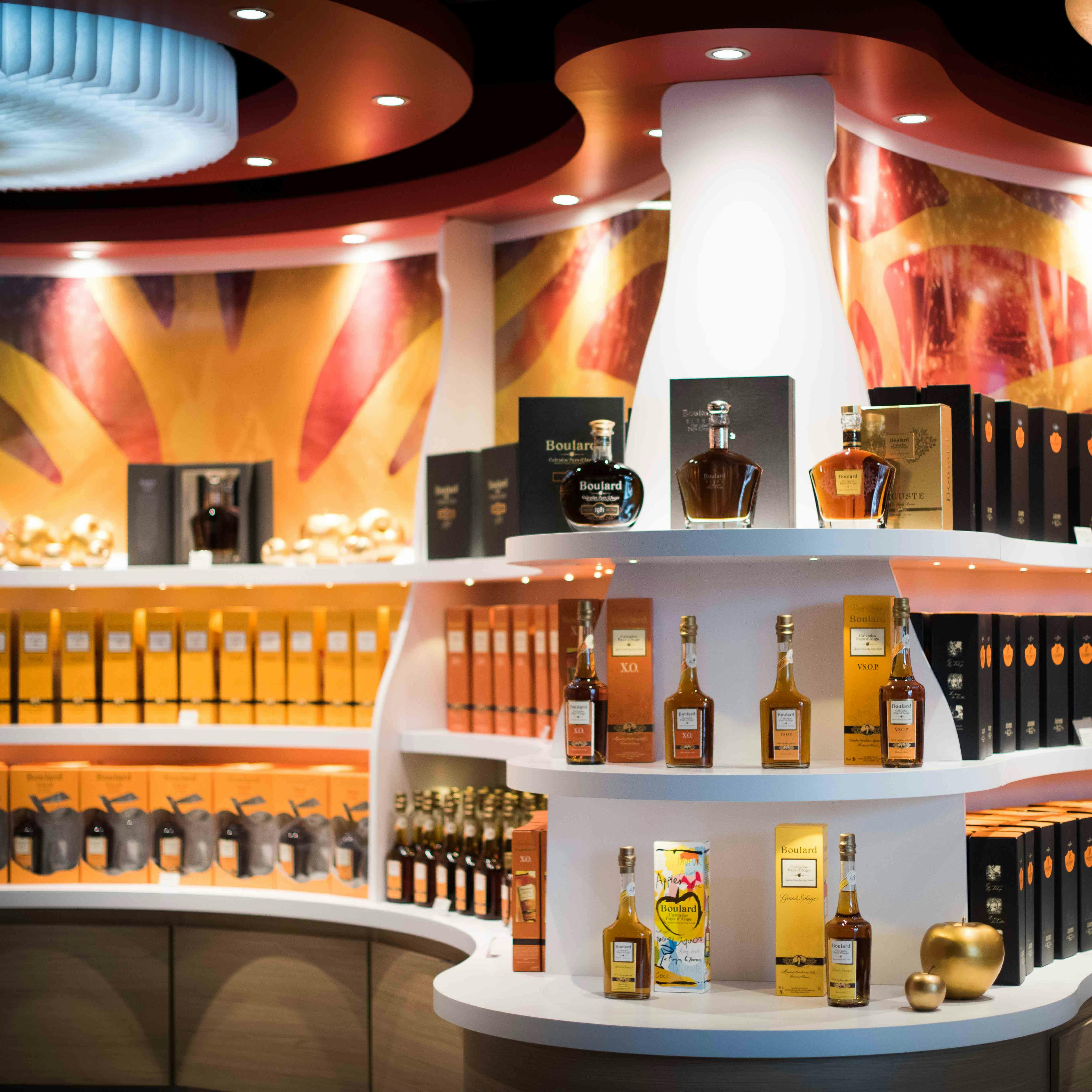 Een helder verlichte slijterij met schappen met verschillende flessen en dozen alcohol, tegen een kleurrijke, abstracte achtergrond.