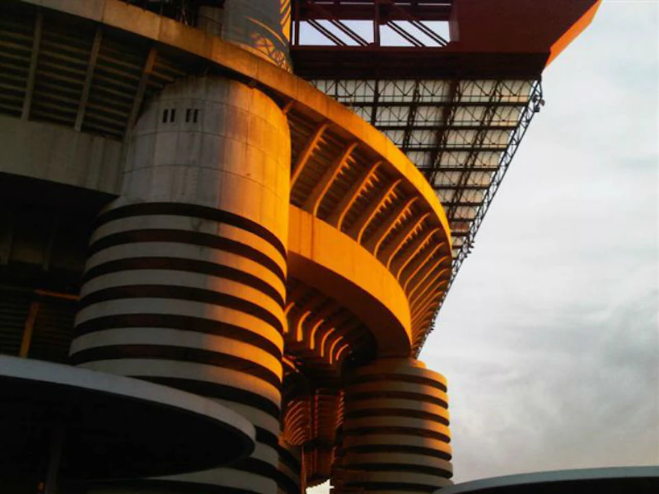 Close-up of a stadium structure with cylindrical columns featuring black and white stripes, under a canopy during sunset.
