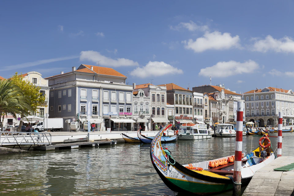 Colorful boats docked along a canal with historic buildings in the background under a partly cloudy sky.