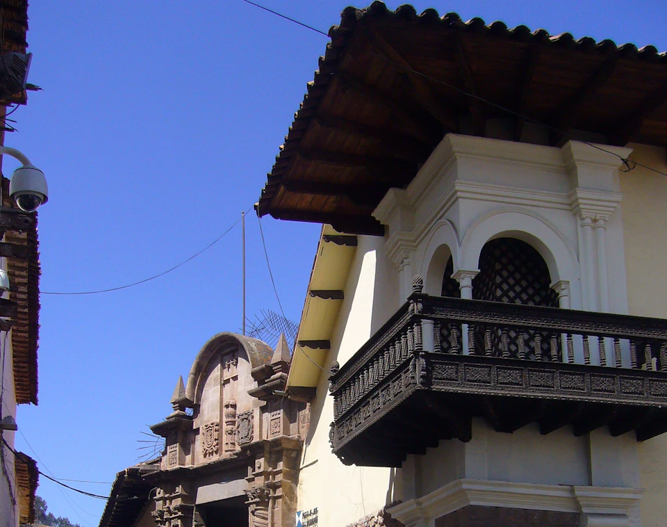 Colonial-style buildings with ornate wooden balconies and arched windows against a clear blue sky.