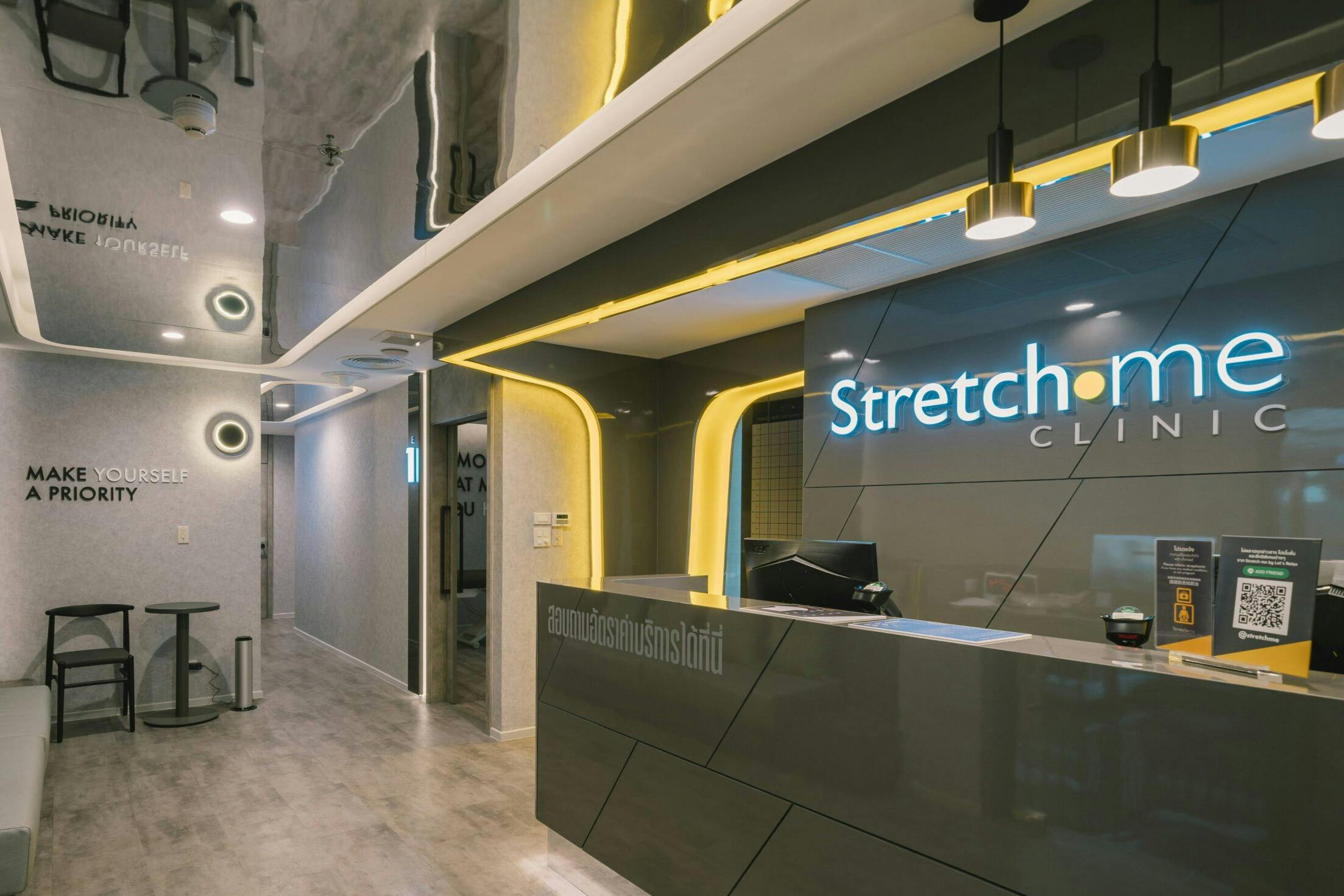 Modern reception area with a desk, illuminated "Stretch" sign, and sleek design elements, featuring yellow lights and gray tones.