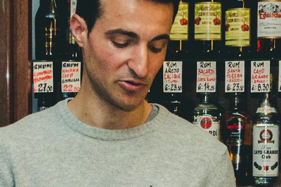 A group of people in a store lined with bottles, with one person holding a plate of food and speaking to the others.