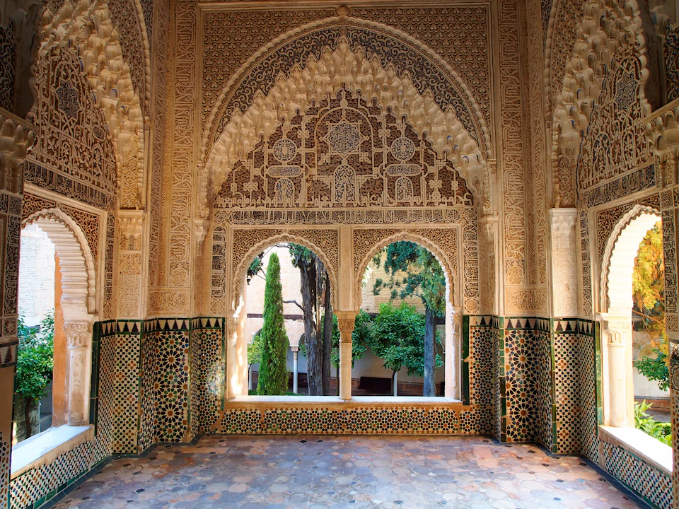 Intricately decorated arched windows with elaborate carvings and colorful tilework, framing a view of trees and greenery outside.
