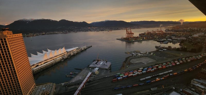 日落时分，鸟瞰带有起重机、集装箱和停泊船只的港口，背景是山脉。